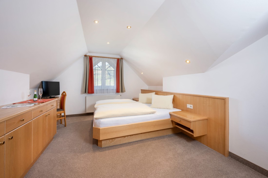 Doppelzimmer mit Dachschräge, Doppelbett, Fernseher und Fenster mit Vorhängen