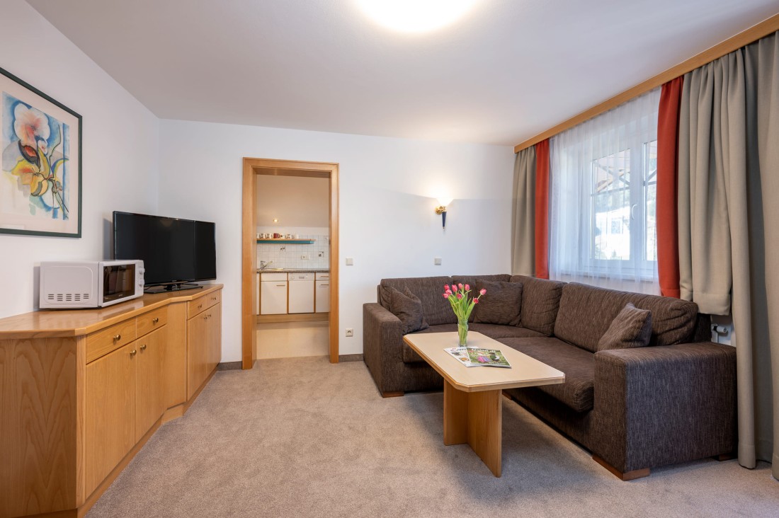 Wohnbereich mit großem Sofa, Couchtisch, Fernseher und Blick in die Küche